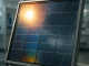 A perovskite-silicon tandem solar panel in a climate-testing lab, reflecting sunlight and rain.